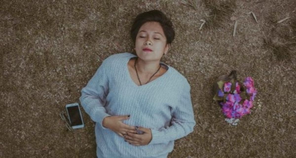 Mädchen im Gras. Foto: unsplash.com | Cristian Newman. Mädchen liegt im Gras, neben sich ein Handy und ein Blumenstrauß.