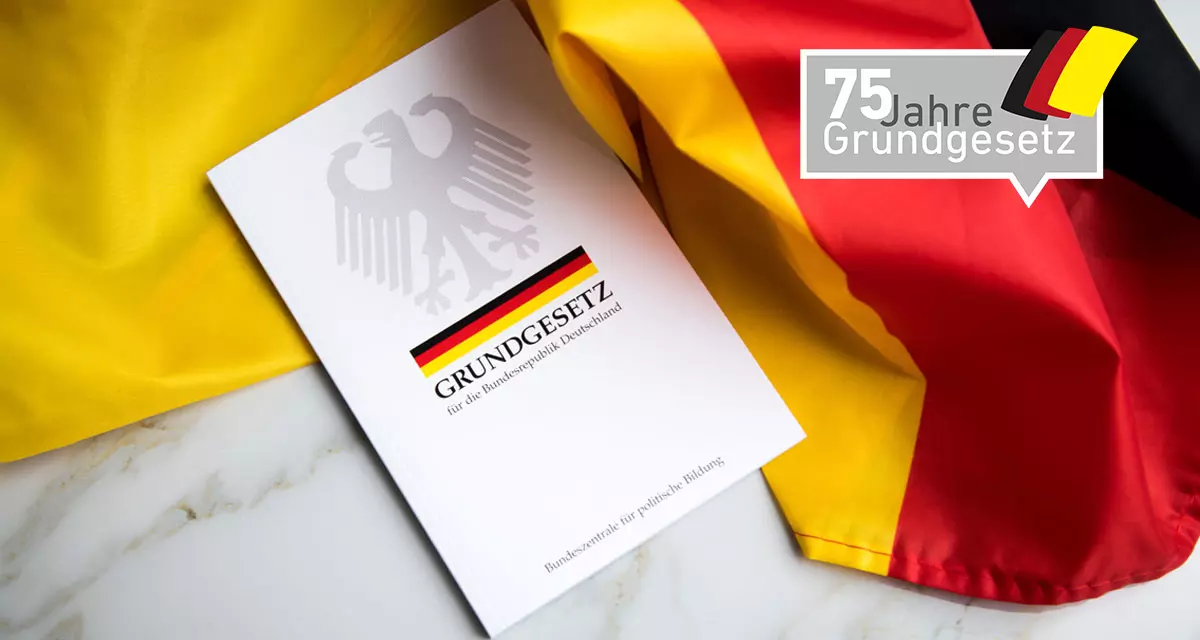 Grundgesetz-Buch der Bundesrepublik Deutschland auf Flagge.  Foto: Adobe Stock | Christin Klose. Logo 75 Jahre Grundgesetz. Grafik: LpB