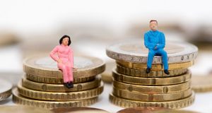 Die Figuren eines Mannes und einer Frau sitzen auf ungleichen Stapeln aus GeldmÃ¼nzen. Foto: picture alliance | Andrea Warnecke. 