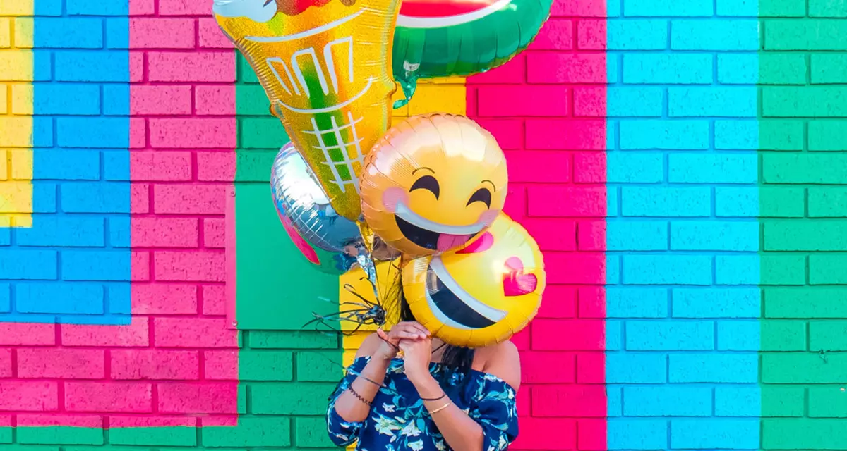 MÃ¤dchen vor farbiger Hauswand mit bunten Luftballons vor dem Gesicht