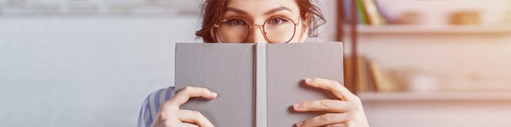 Frau mit Brille hinter einem Buch. Foto: Adobe Stock
