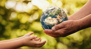 HÃ¤nde eines Ã¤lteren Menschen reichen eine Weltkugel an KinderhÃ¤nde.