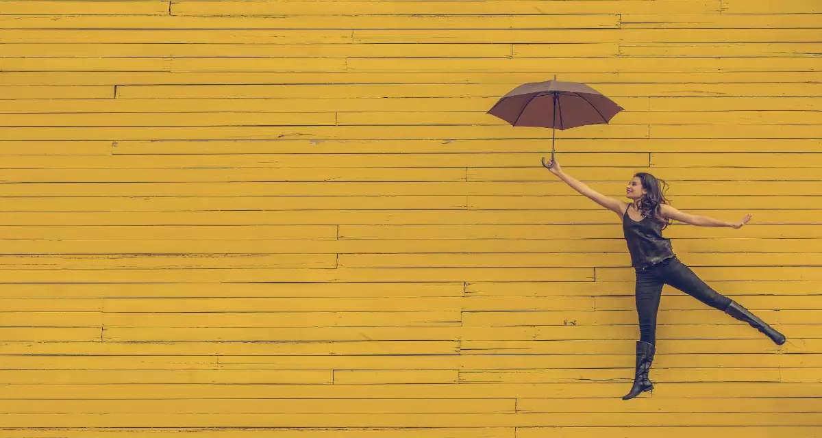 MÃ¤dchen mit Regenschirm vor gelber Wand.  