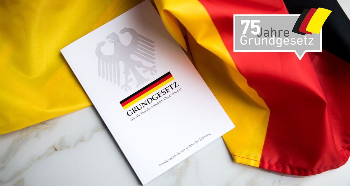 Grundgesetz-Buch der Bundesrepublik Deutschland auf Flagge. Foto: Adobe Stock | Christin Klose. Logo 75 Jahre Grundgesetz. Grafik: LpB