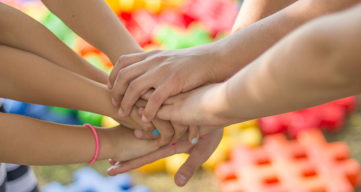 Kinderhände Übereinandergelegte Kinderhände vor buntem Hintergrund.